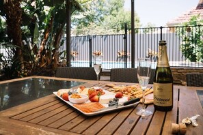 Une table en bois sur laquelle se trouvent une bouteille de Prosecco, un verre et un plateau de nourriture comprenant des fraises, du fromage et des crackers.