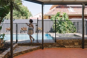 A covered outdoor area with a swimming pool, stone steps, and a metal fence.