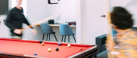 Une table de billard avec des billes, dans une pièce meublée dans un style moderne, avec une porte visible au fond.