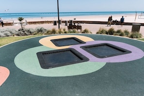 A playground with three trampolines and a bench near a beach.