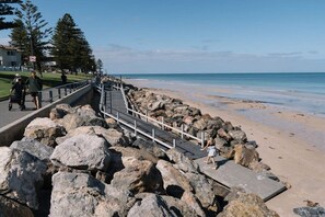 A coastal walkway with a rocky barrier, a pedestrian path, and a beach in the background.