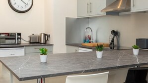 A modern kitchen with a central island, stainless steel appliances, and a clock on the wall. - Bright & Contemporary 1bedroom Annexe - Herne Hill! (London)