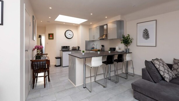 A modern kitchen with a central island, bar stools, and a dining area with a table and chairs. - Bright & Contemporary 1bedroom Annexe - Herne Hill! (London)