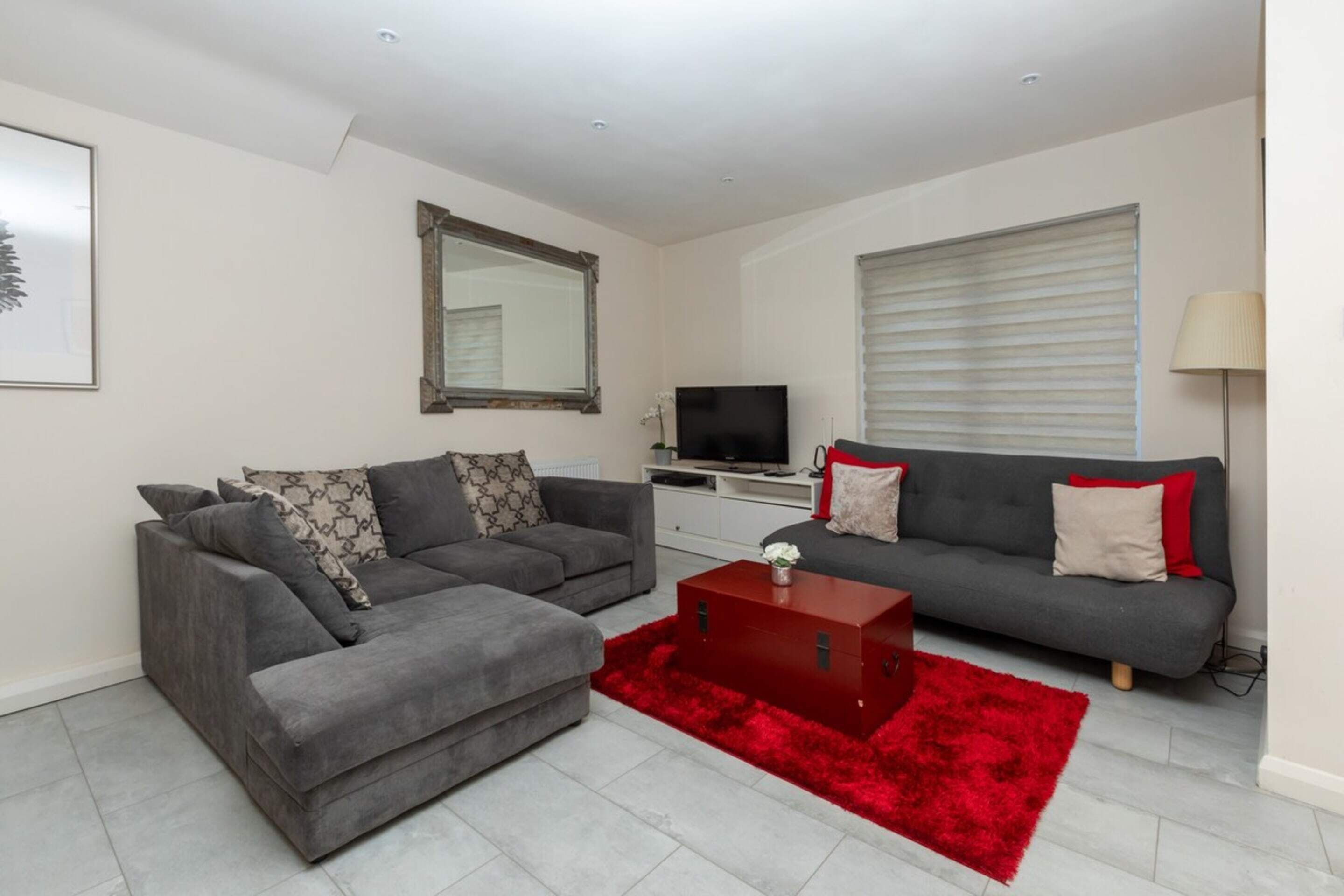 Ein modernes Wohnzimmer mit zwei grauen Sofas, einem roten Couchtisch und einem Fernseher.
