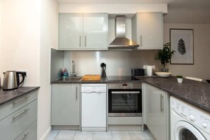 Una cocina moderna con armarios blancos, lavavajillas, horno y lavadora.