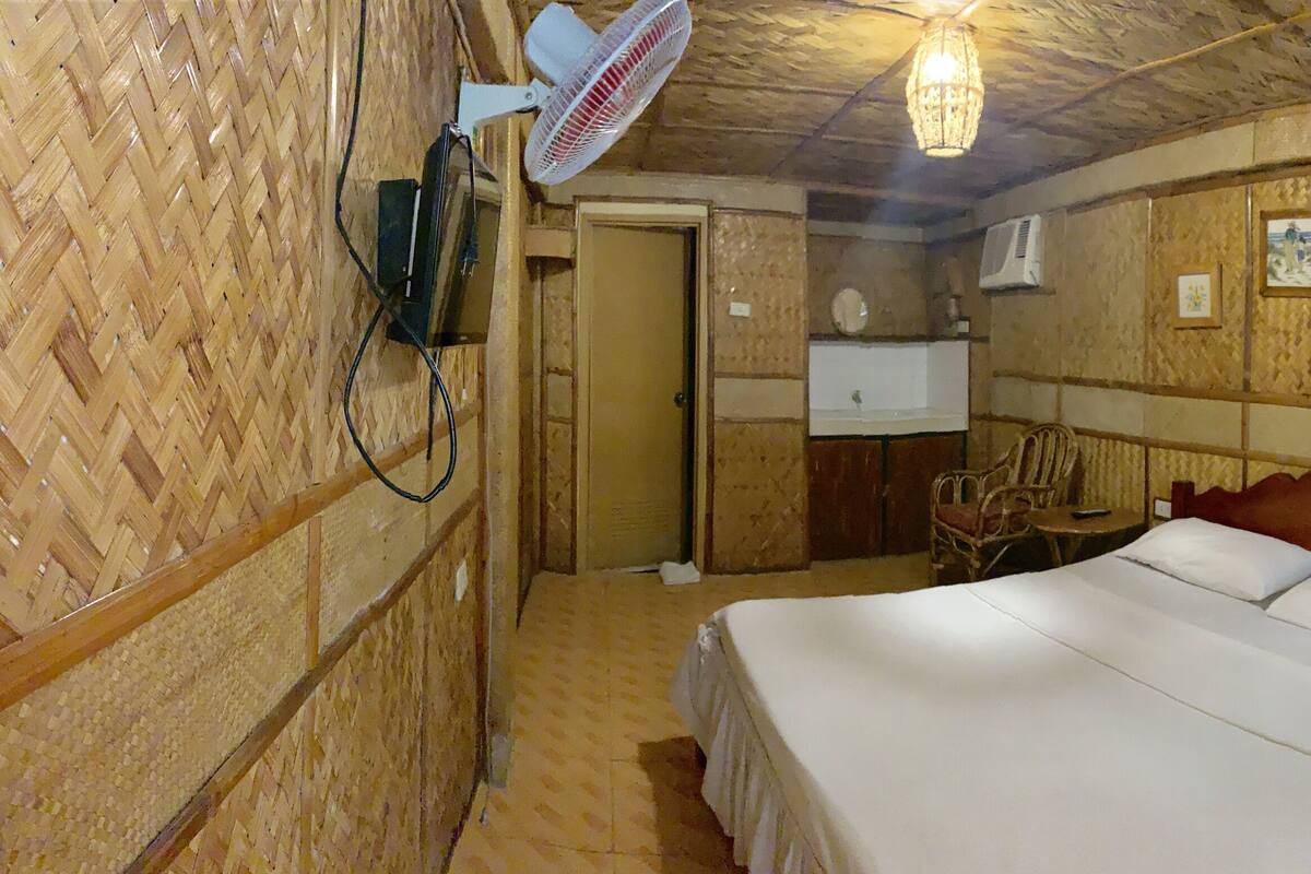 A room with a bed, a chair, a desk, and a fan.