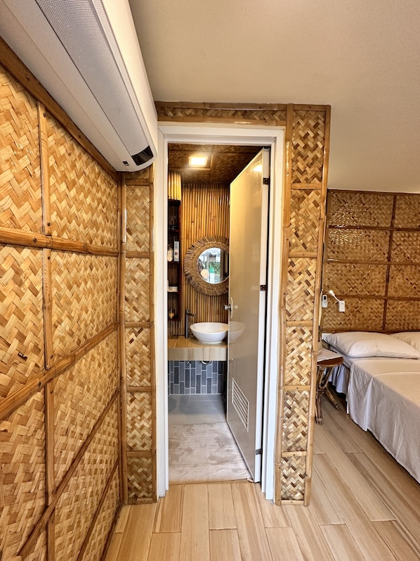 A room with a bamboo-patterned wall, a round mirror, a sink, and a bed.
