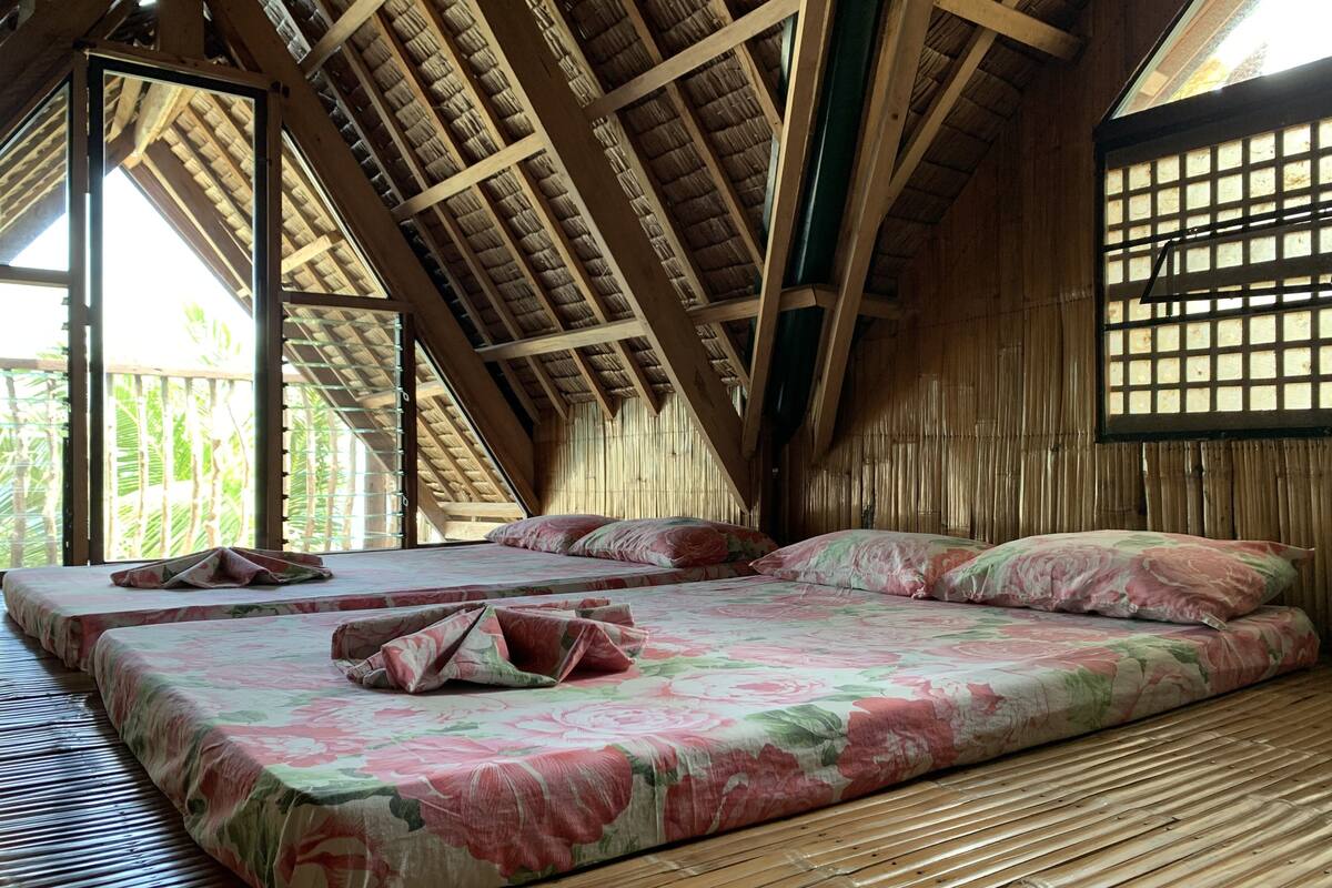 A room with a sloped ceiling, wooden beams, a bed with floral bedding, and a bamboo floor.
