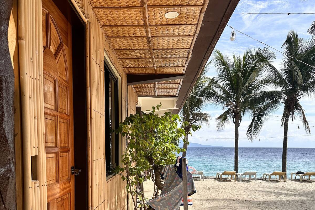 A beachside building with a wooden door, a thatched roof, and a view of the ocean.