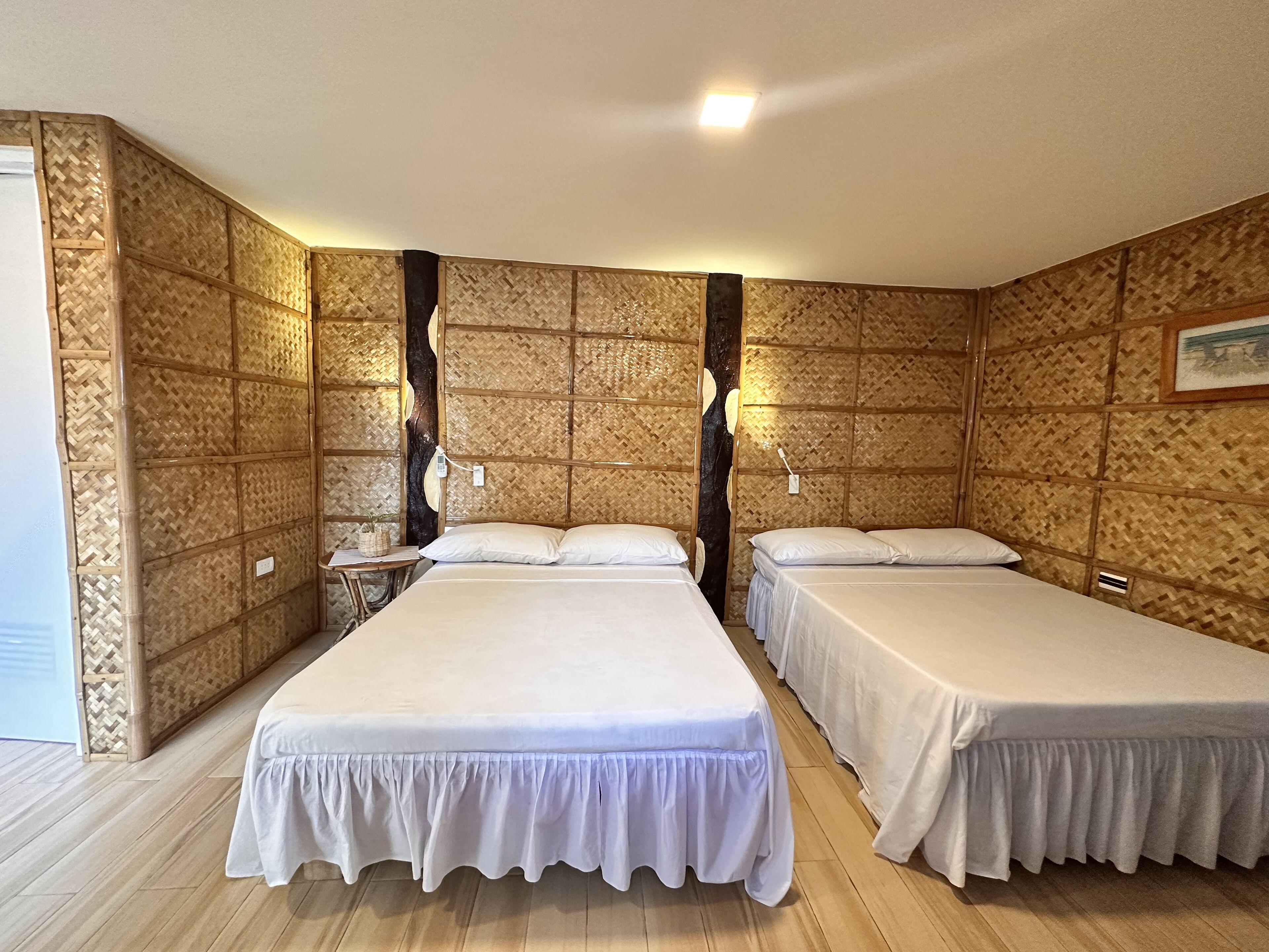 Ein Zimmer mit zwei Betten, einem Nachttisch, einer Wandleuchte und Holzboden.