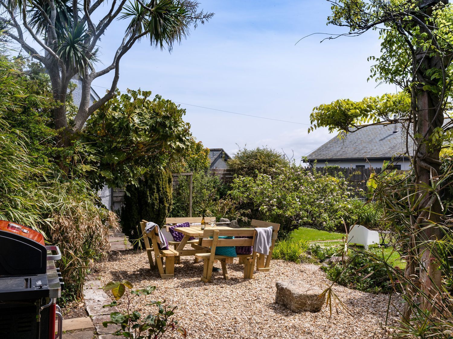 A garden with a wooden table and chairs, surrounded by gravel and greenery.