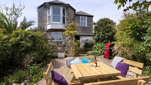 A stone house with a bay window, a wooden table with benches, and a barbecue grill in the garden. - Ayr Farmhouse (St Ives)