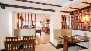Una biblioteca accogliente con scaffali in legno, posti a sedere comodi e un tavolo da biliardo.