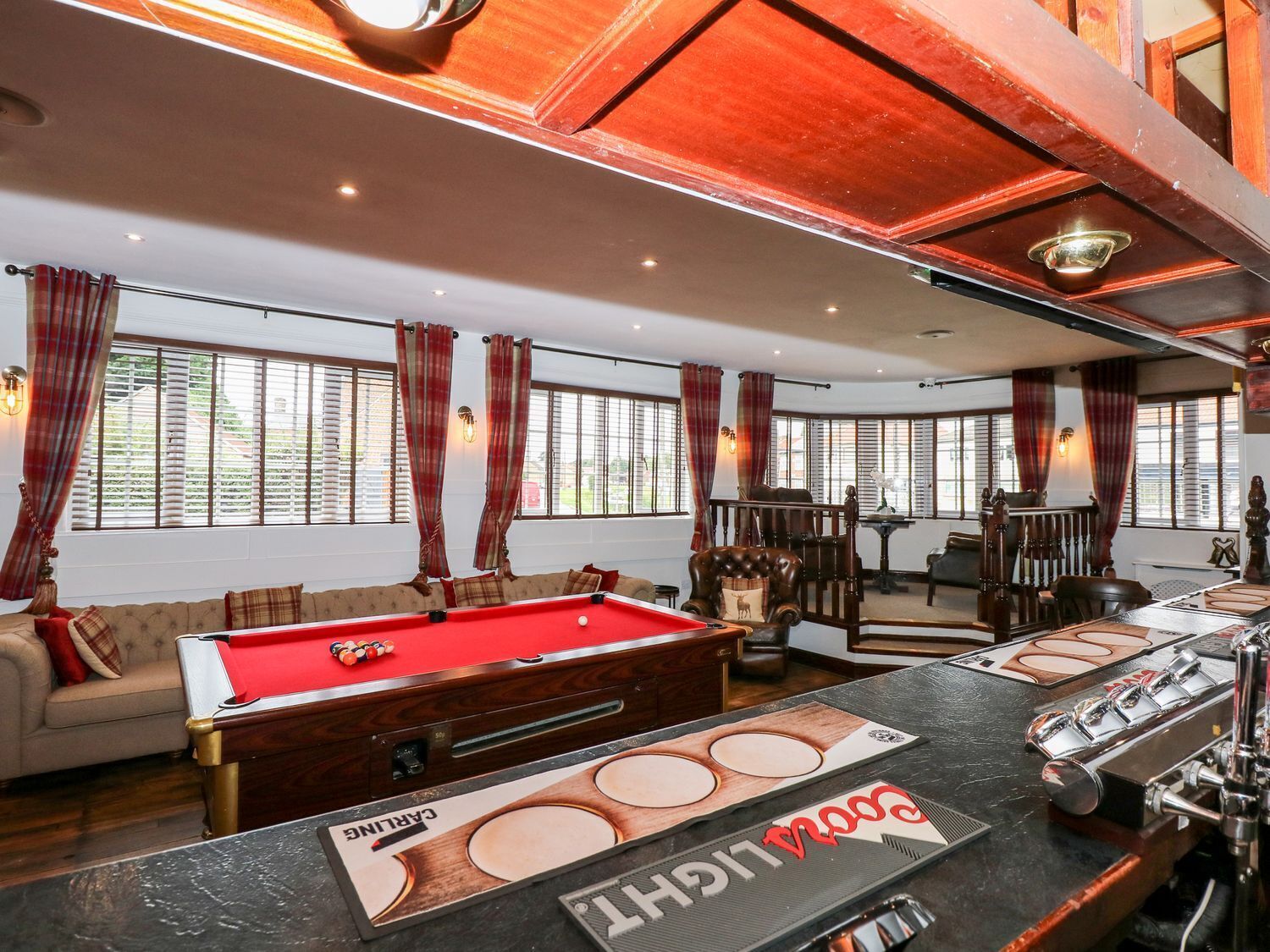 A pool table with a billiard cue, a bar area with a beer tap, and a seating area with a sofa and armchairs.