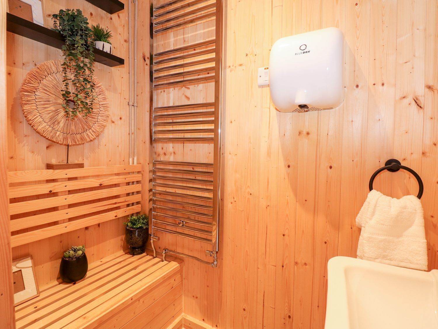 A wooden sauna room with a bench, a towel rack, and a wall-mounted towel dispenser.