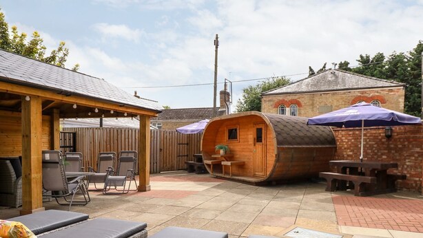 Un'area patio con poltrone relax, una struttura a botte in legno e una zona salotto coperta.
