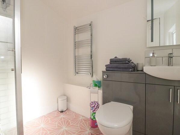 A bathroom with a toilet, a sink, a towel rack, and a trash bin. - The Potting Shed (Langport)