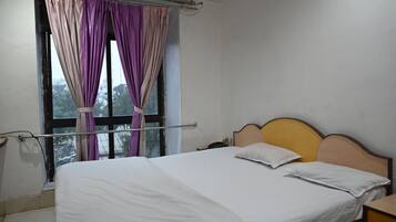 A single bed with a wooden headboard, a bedside table, and a window with purple curtains.