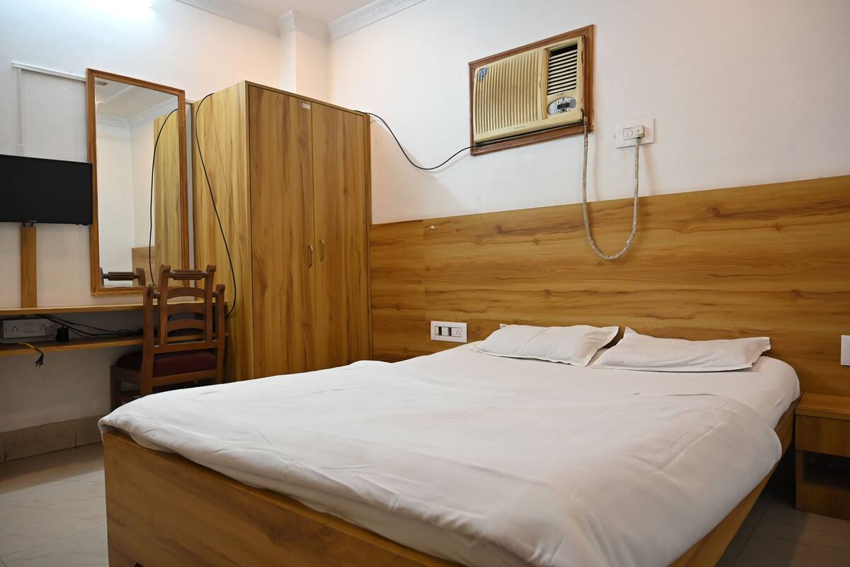A bedroom with a wooden bed, a wooden wardrobe, a mirror, a desk, and a wall-mounted air conditioner.