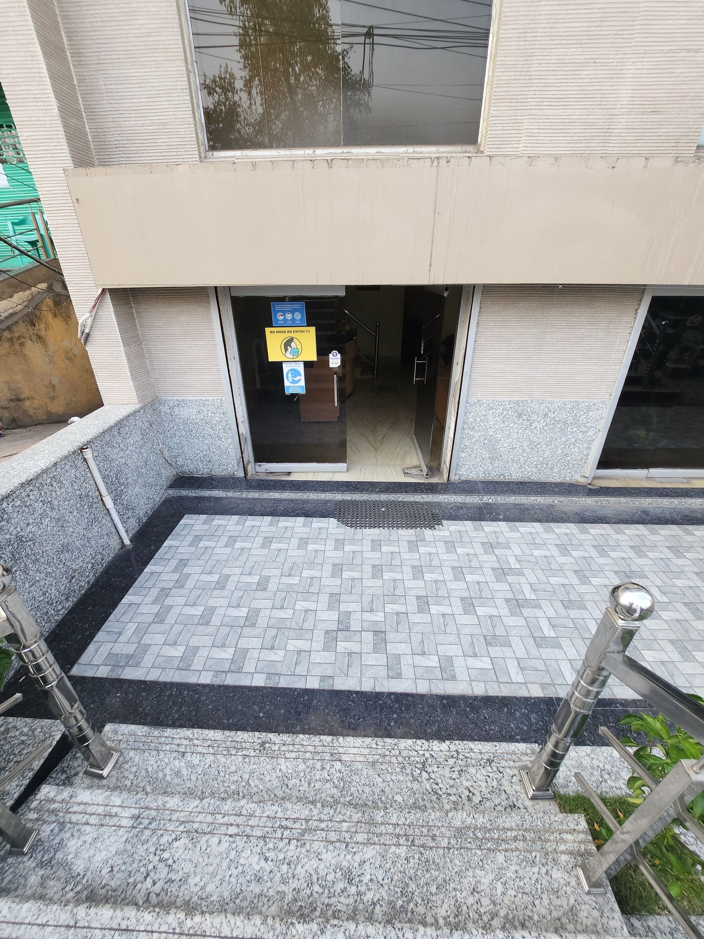 A building entrance with a tiled pathway leading to a door. There are signs indicating no mask entry and a no smoking policy.