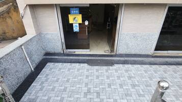 A building entrance with a tiled pathway leading to a door. There are signs indicating no mask entry and a no smoking policy.