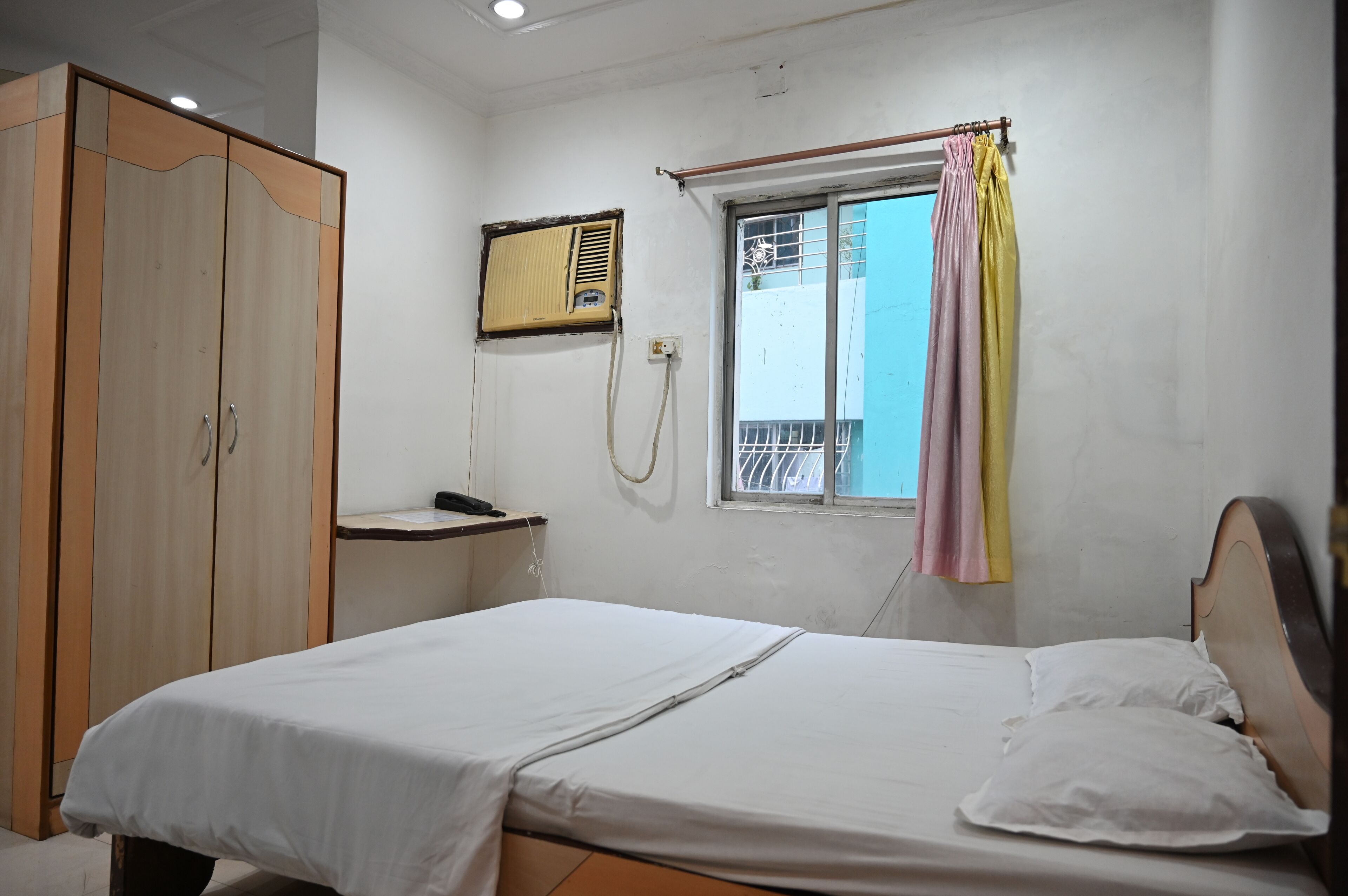 A bedroom with a bed, a wardrobe, a window with curtains, and a wall-mounted air conditioner.