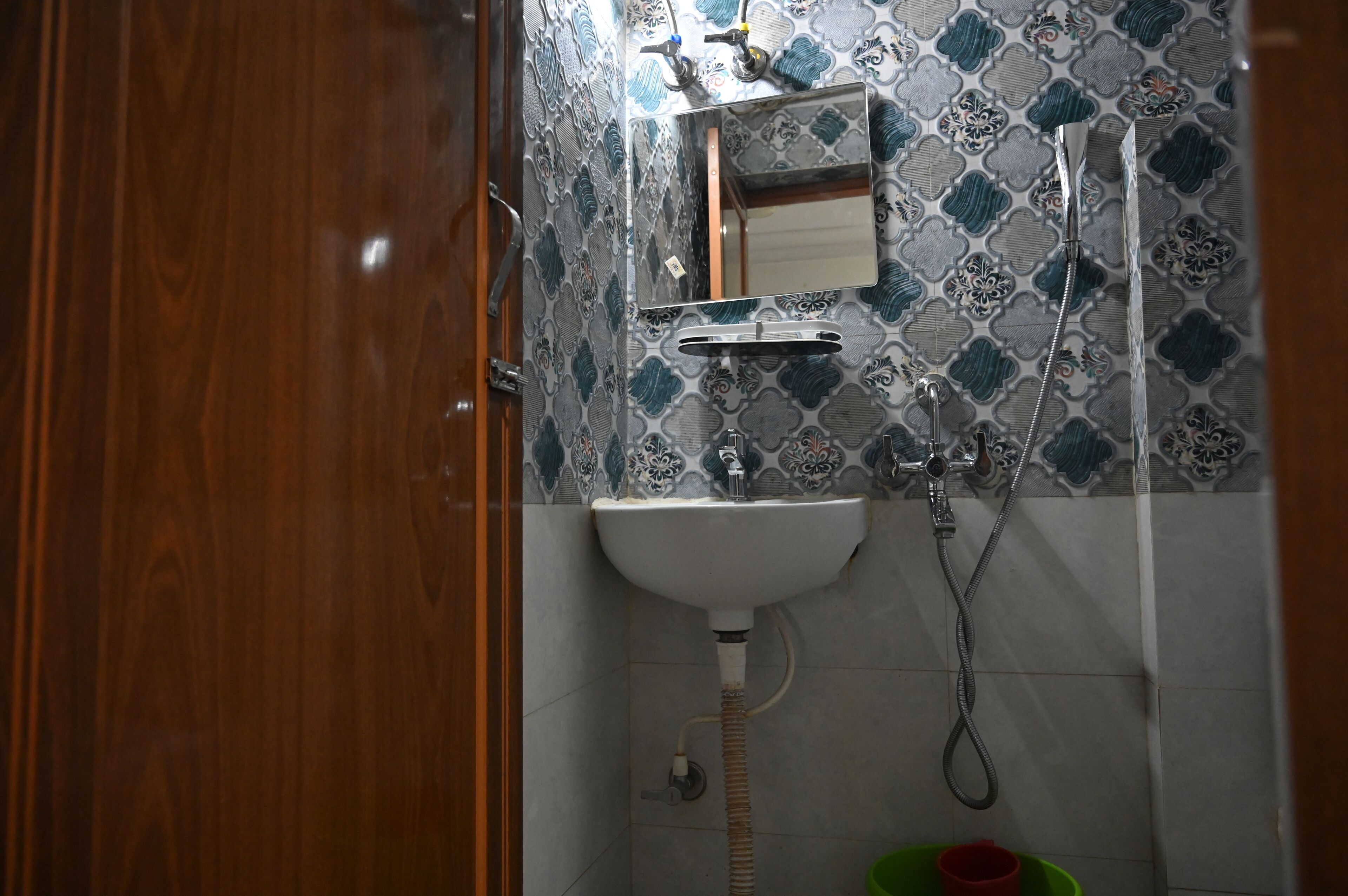Un baño con puerta de madera, un lavabo blanco, un espejo, ducha y azulejos estampados.