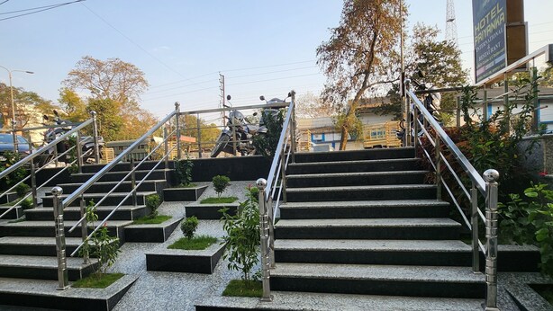 Escadas externas com corrimão de metal, rodeadas por pequenos vasos e um caminho pavimentado.