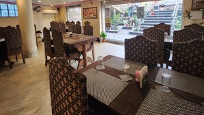 Um restaurante com cadeiras e mesas estampadas, um pilar grande e vista para a rua.