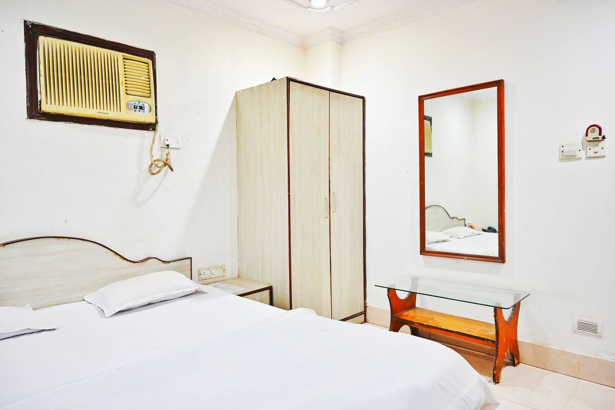 A hotel room with a bed, a wardrobe, a bedside table, a mirror, and a radiator.