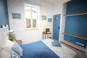 Un dormitorio con una cama, un escritorio con una computadora portátil, una ventana y una puerta.