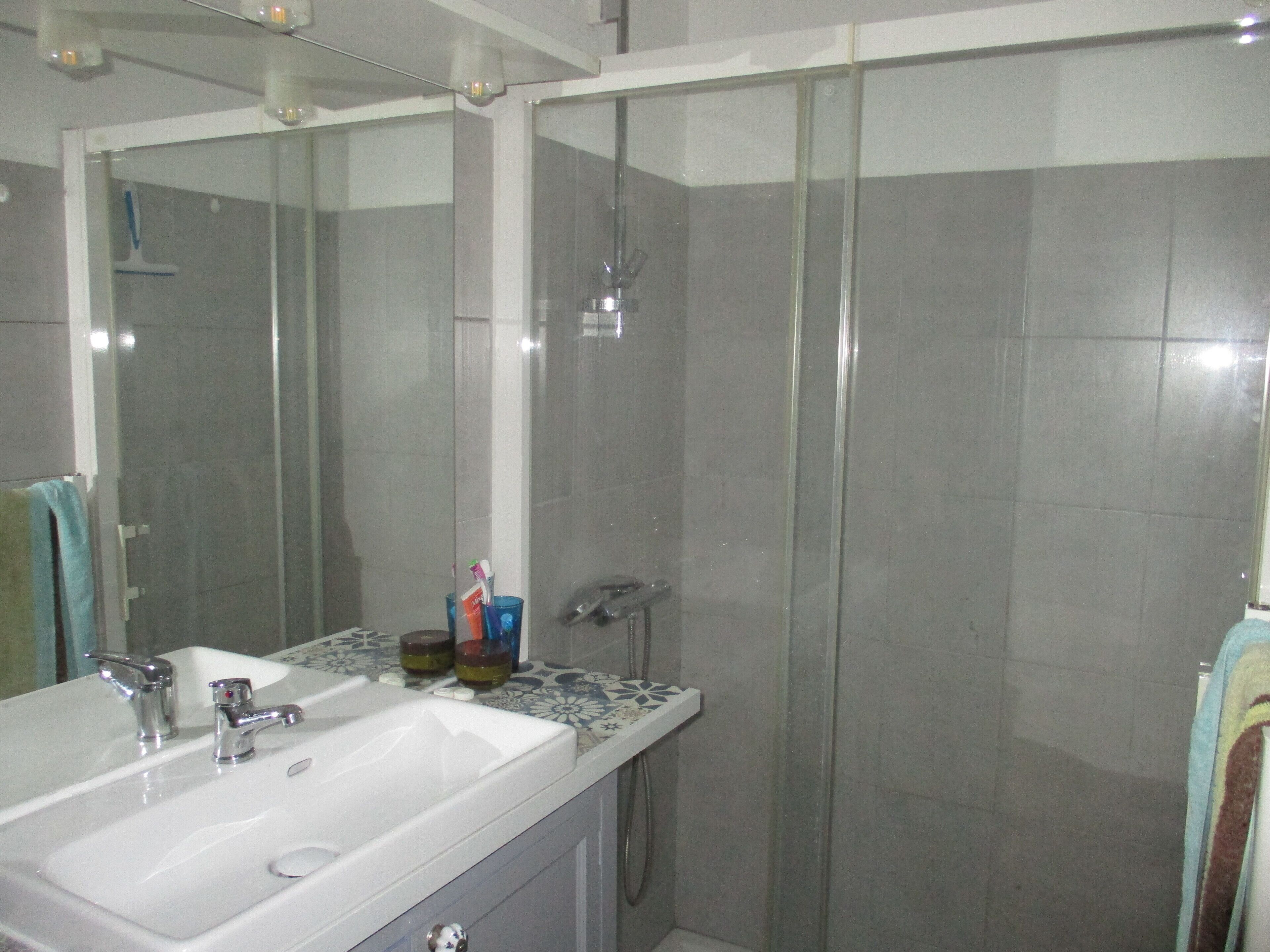 Un baño con un lavabo blanco, dos grifos, una cabina de ducha de vidrio y un espejo.