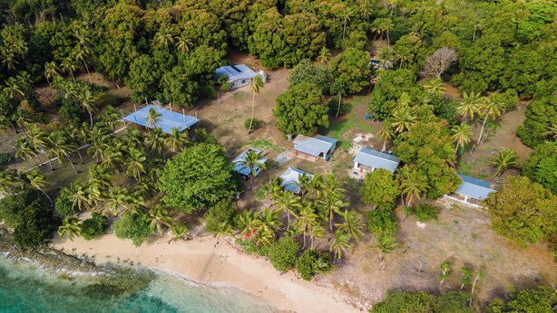 Vue aérienne d’un complexe hôtelier tropical, avec plusieurs bâtiments entourés d’une végétation luxuriante de palmiers et une plage.