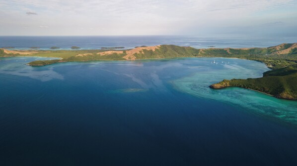 An aerial view of a coastal area with clear blue waters, green hills, and small islands. - Yawekata Eco Still Bluewater Lodge (Naviti Island)