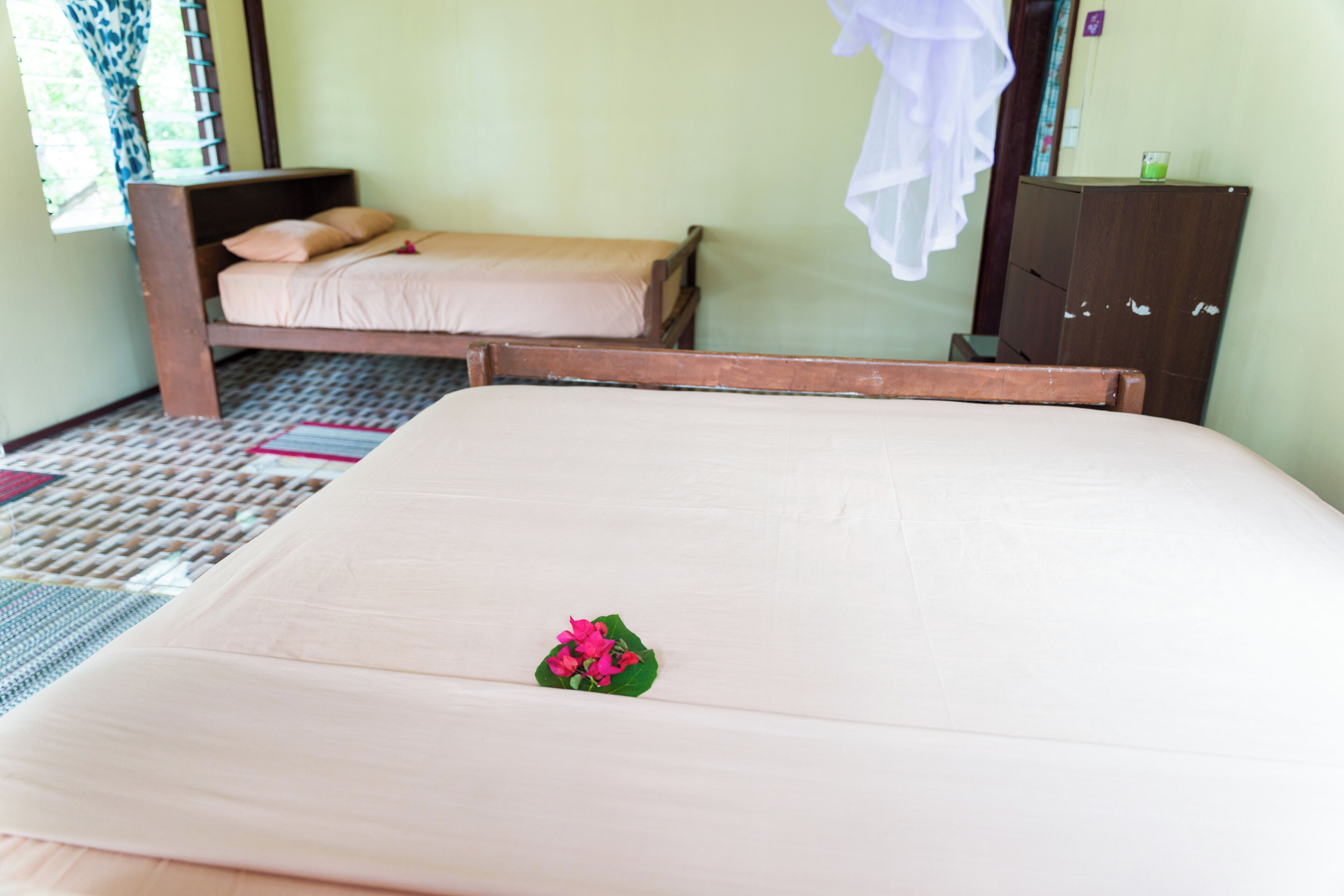 A room with two beds, one with a canopy and another without. There is a wooden cabinet and a small table with a glass.