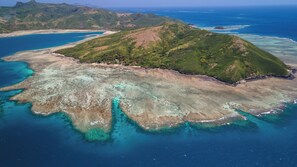 An aerial view of a tropical island with clear blue waters, green vegetation, and a small beach area. - Yawekata Eco Still Bluewater Lodge (Naviti Island)