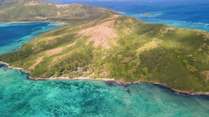 Vue aérienne d’une île tropicale aux eaux turquoise et limpides, à la végétation luxuriante et verdoyante, et à un petit village avec des bâtiments situés près de la côte.