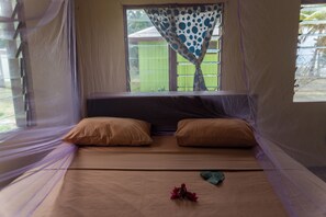A bed with two pillows, a window with a curtain, and a mosquito net. - Yawekata Eco Still Bluewater Lodge (Naviti Island)