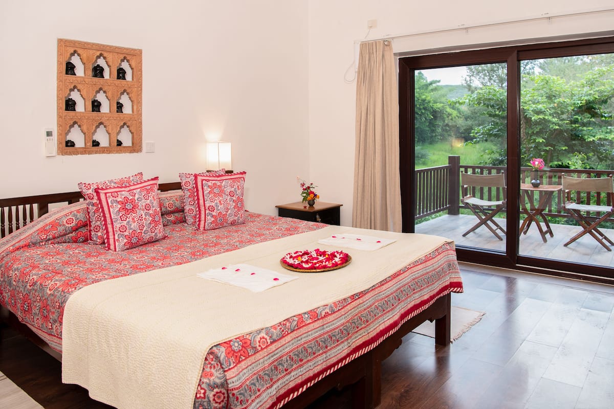 Un dormitorio con una cama grande, una mesita de noche, una ventana con vistas al exterior y una puerta corrediza que da a un balcón.
