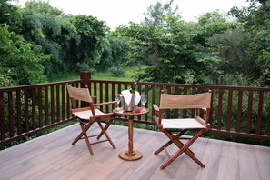 Eine Holzterrasse mit zwei Klappstühlen und einem Tisch, umgeben von einem Hollergeländer und üppiger Bepflanzung.