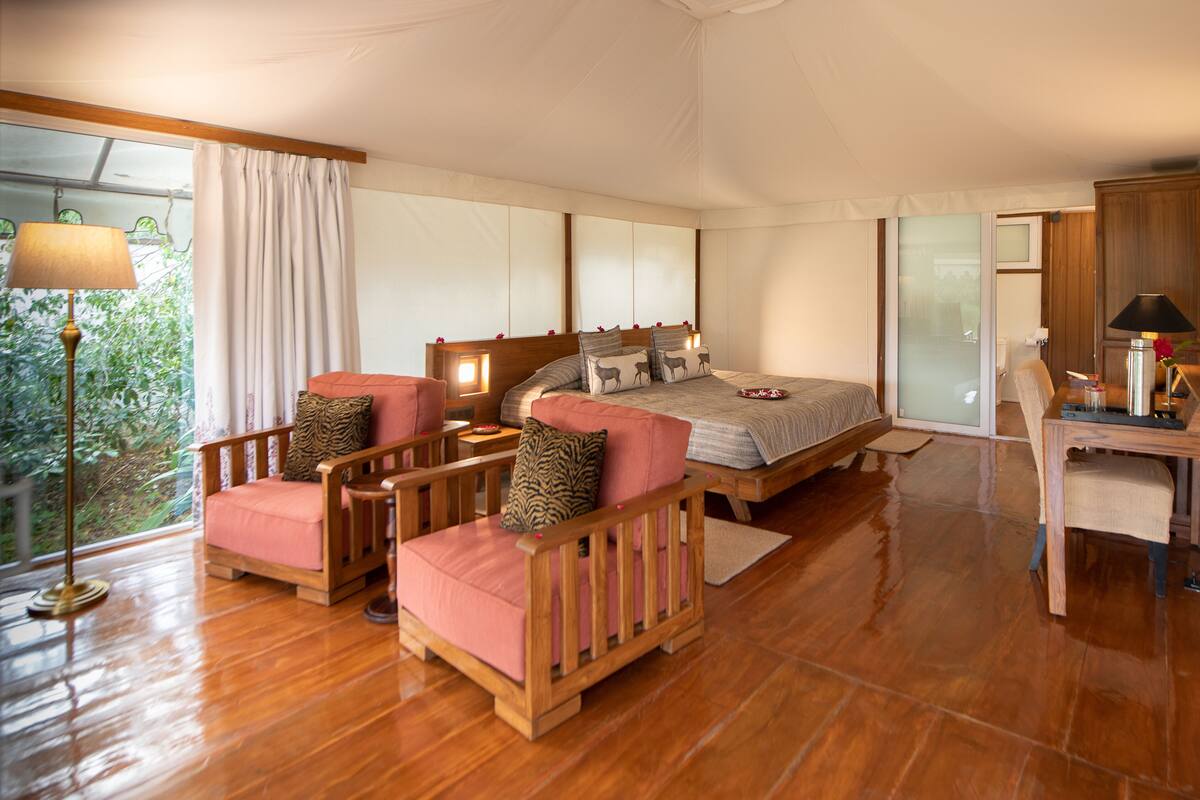 Un dormitorio con cama, dos sillas de madera, un escritorio y un ventanal con cortinas.