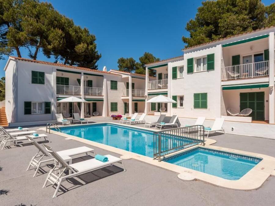 Un espace piscine doté de chaises longues et de parasols, entouré d’immeubles à plusieurs étages avec des balcons.