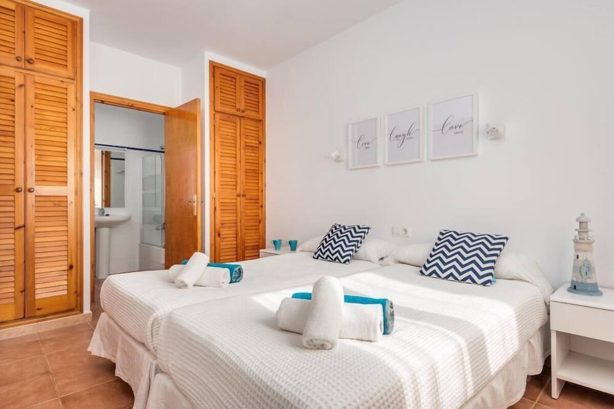Une chambre d’hôtel avec un lit, deux oreillers, une table de chevet, un mur orné de tableaux et une porte en bois.