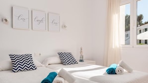 Habitación de hotel con dos camas, cada una con una toalla enrollada, un adorno de faro y tres citas inspiradoras enmarcadas en la pared.