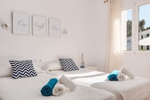 Habitación de hotel con dos camas, cada una con una toalla enrollada, un adorno de faro y tres citas inspiradoras enmarcadas en la pared.