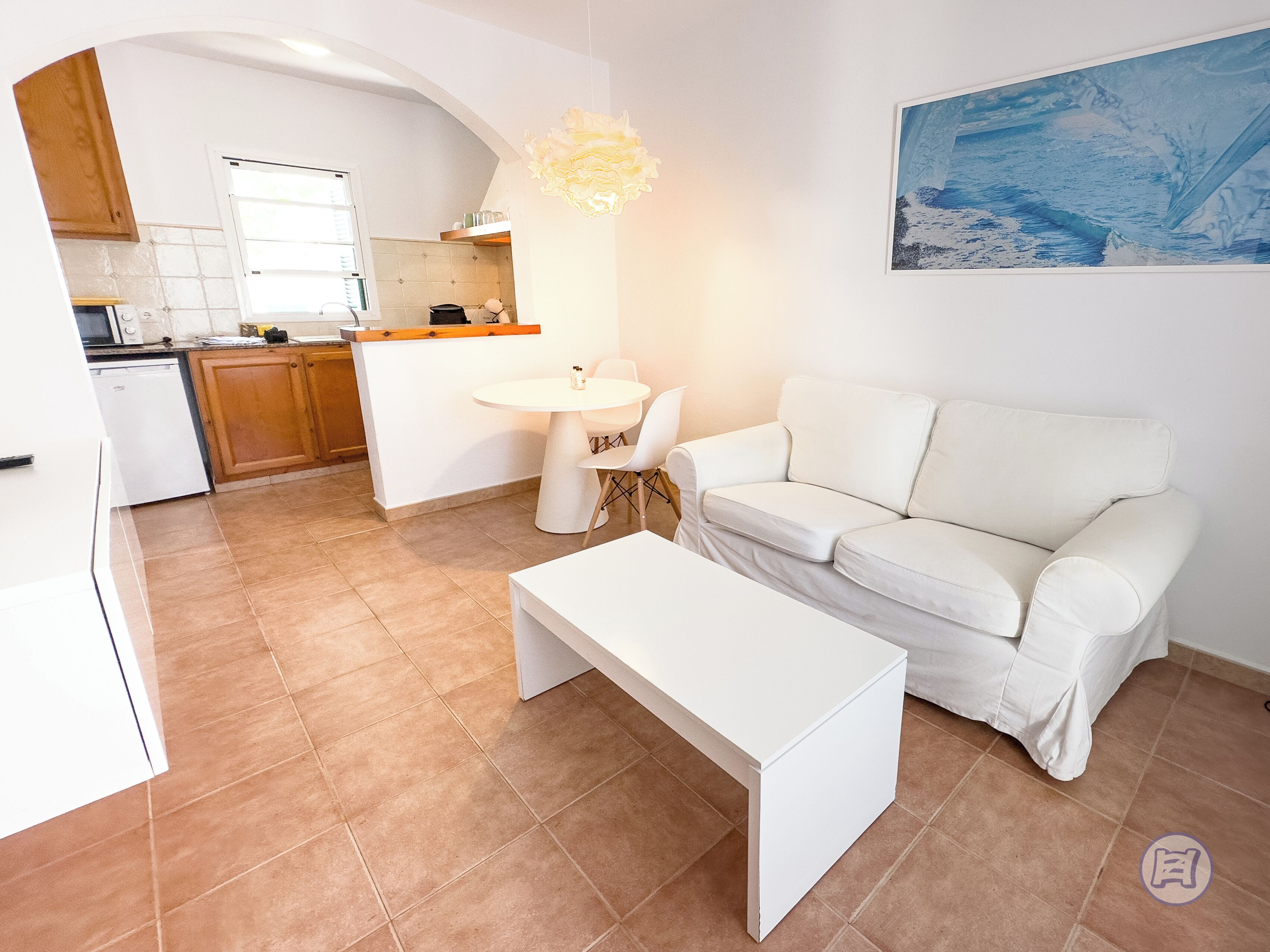 Una sala de estar moderna con un sofá blanco, una mesa de centro blanca y un comedor con una mesa y sillas blancas.