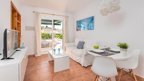 Una sala de estar moderna con un sofá blanco, una mesa de comedor para dos personas y un televisor sobre un mueble blanco.