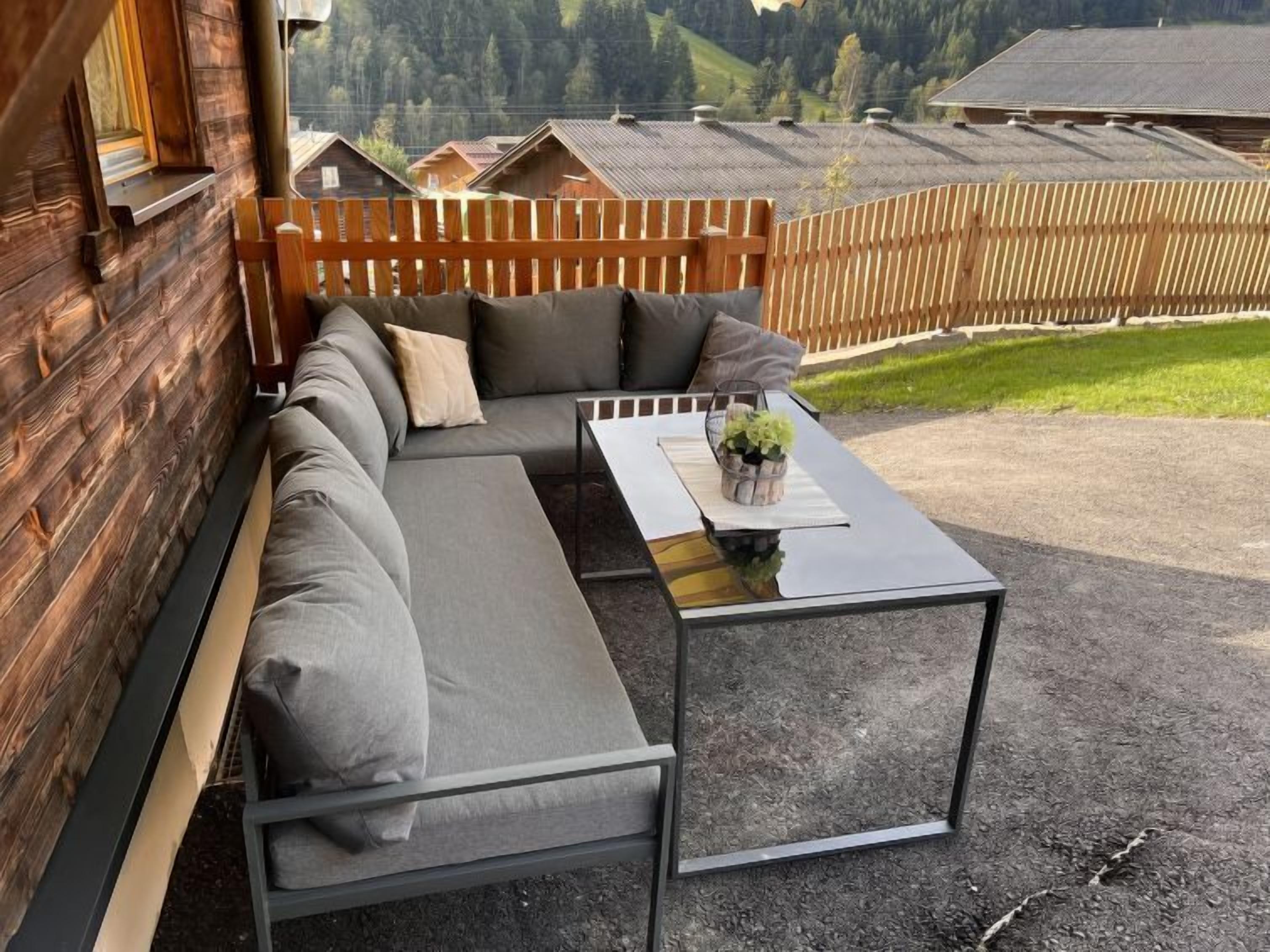 A wooden cabin with a built-in sofa and a glass table, overlooking a mountainous landscape.