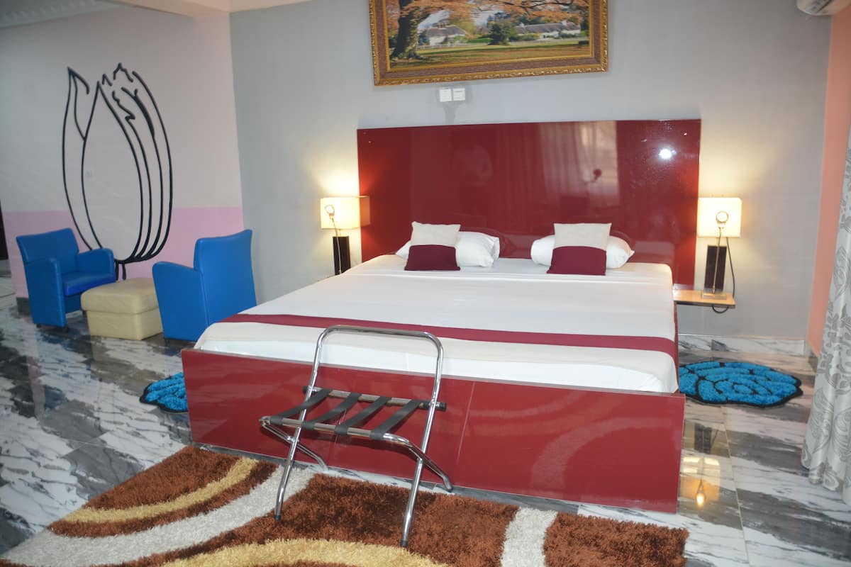 A hotel room with a large bed, two bedside tables with lamps, a red headboard, a blue chair, and a brown and white striped rug.