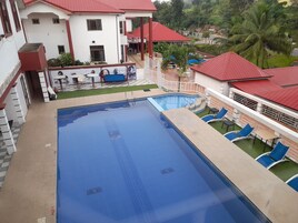 Piscina com borda xadrez, rodeada por espreguiçadeiras e uma pequena área de deck.